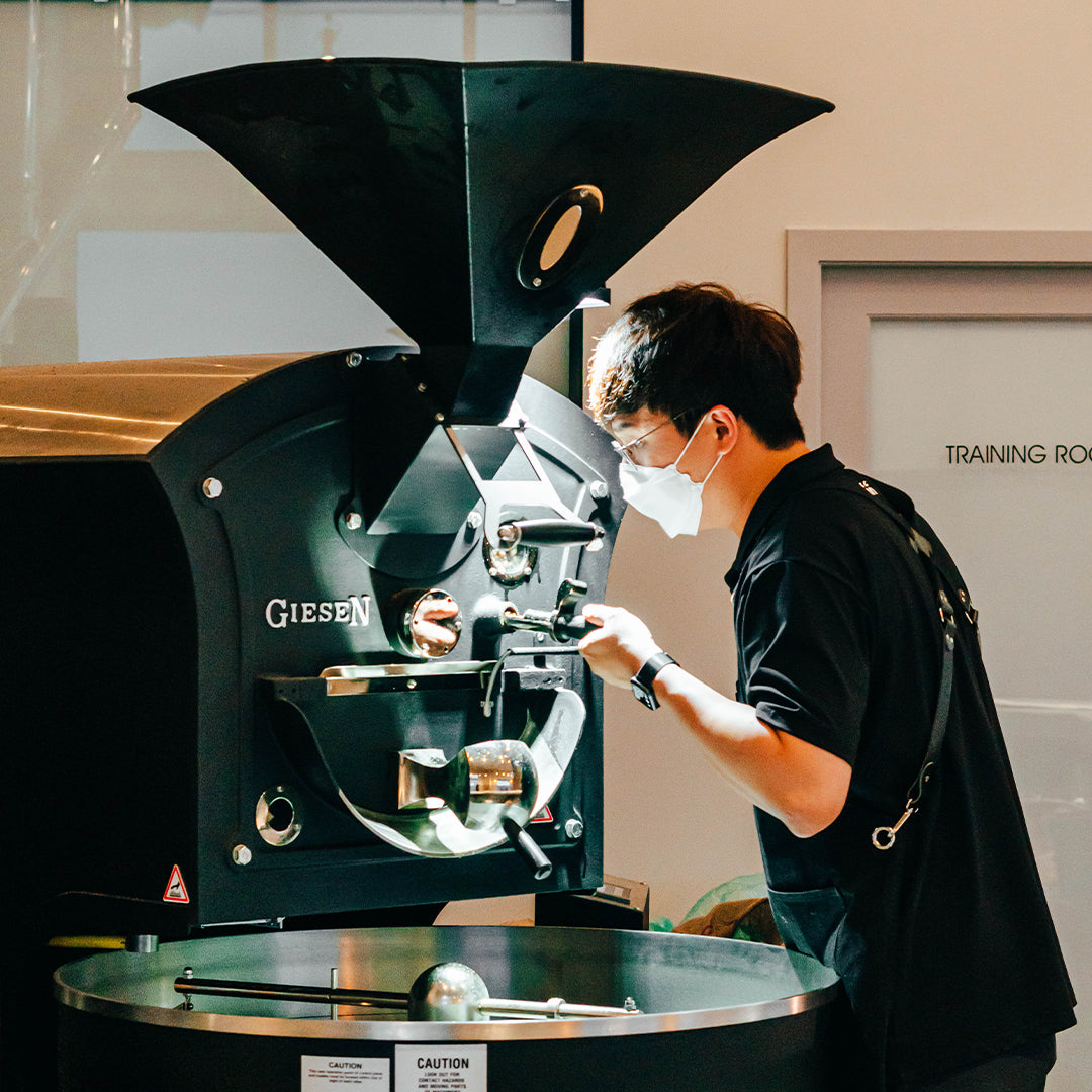 A professional inspecting a coffee roasting machine, ensuring proper functionality and quality control for optimal performance in the café setting. This image highlights the attention to detail and expertise that supports ongoing training and machine maintenance for consistent coffee quality.