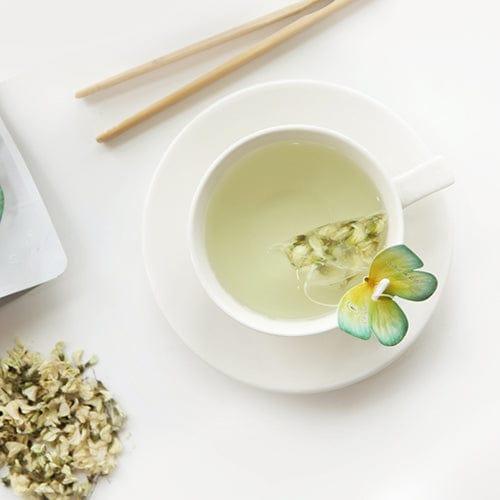 Side view of a cup of tea with a butterfly-shaped tea bag hanging from the edge, gently resting on the rim.