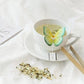 Side view of a cup of tea with a butterfly-shaped tea bag resting elegantly on the edge, the steam rising gently from the cup.