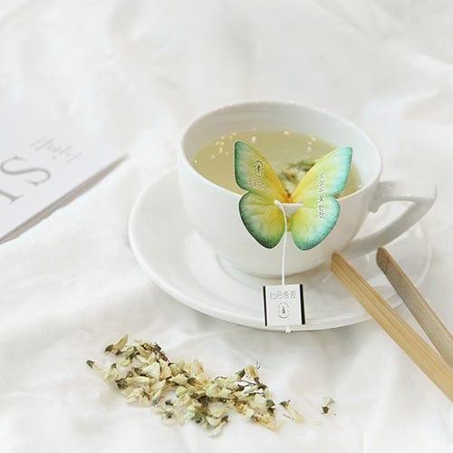 Side view of a cup of tea with a butterfly-shaped tea bag resting elegantly on the edge, the steam rising gently from the cup.