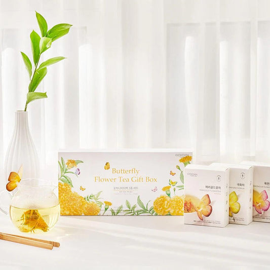 A top-down view of the Butterfly Flower Tea Gift Set (Yellow), featuring the neatly packaged box and its contents. The three types of tea bags—Marigold, Magnolia, and Siberian Chrysanthemum—are arranged inside the box, with each tea bag showcasing intricate floral designs. The yellow packaging and butterfly-shaped tea bag holder stand out against the neutral background, emphasizing the elegant presentation and quality of the tea. The set is presented in a clean, sophisticated manner, highlighting its suitab