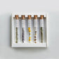 A top-down view of the Assorted Flower Tea Sticks Gift Set, with the glass test tube placed upright in the center. The individually packaged tea sticks are arranged beside the test tube, showcasing their delicate flower shapes. The elegant gift box is partially visible, emphasizing the premium and decorative nature of the set. The background is clean and minimal to highlight the beauty and craftsmanship of the tea sticks.