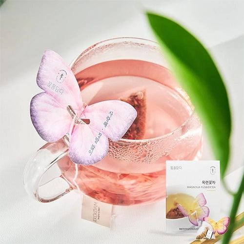 A butterfly-shaped tea bag resting on the edge of a glass filled with Magnolia Butterfly Tea.