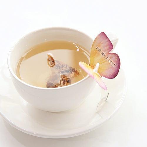 Side view of a glass cup of Magnolia Butterfly Tea with the butterfly-shaped tea bag hanging over the rim.
