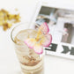 Side view of a clear glass cup filled with Magnolia Butterfly Tea, showcasing the butterfly-shaped tea bag resting on the rim.