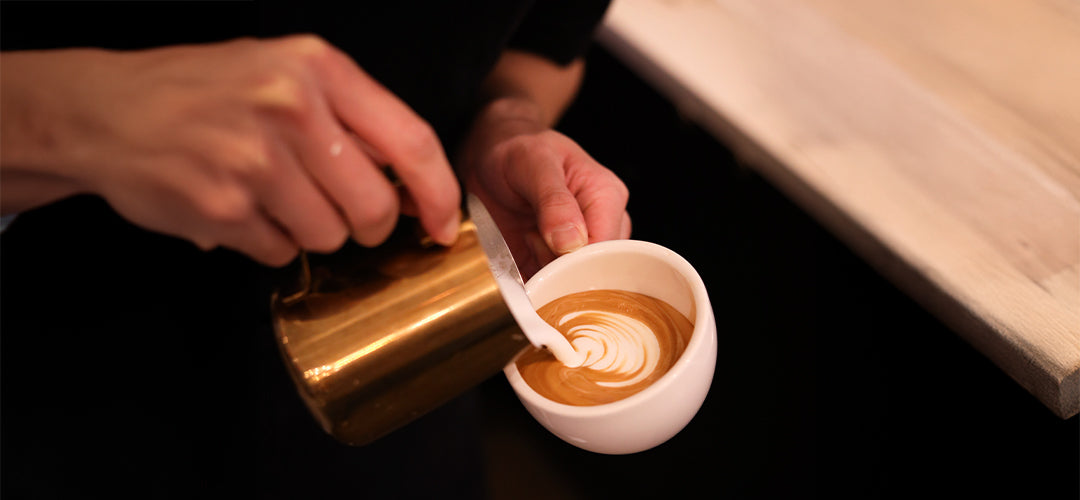 A skilled barista carefully pouring steamed milk into a freshly brewed espresso, creating intricate and beautiful latte art with precision and finesse, showcasing the artistry and craftsmanship at C Market Coffee.