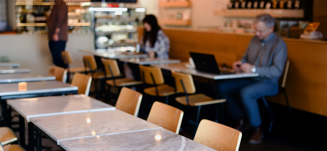 A welcoming café interior at C Market Coffee's Coquitlam location, showcasing a modern design with warm lighting, wooden accents, and cozy seating arrangements. A coffee bar equipped with an on-site roastery and gourmet kitchen creates a vibrant yet relaxed atmosphere.