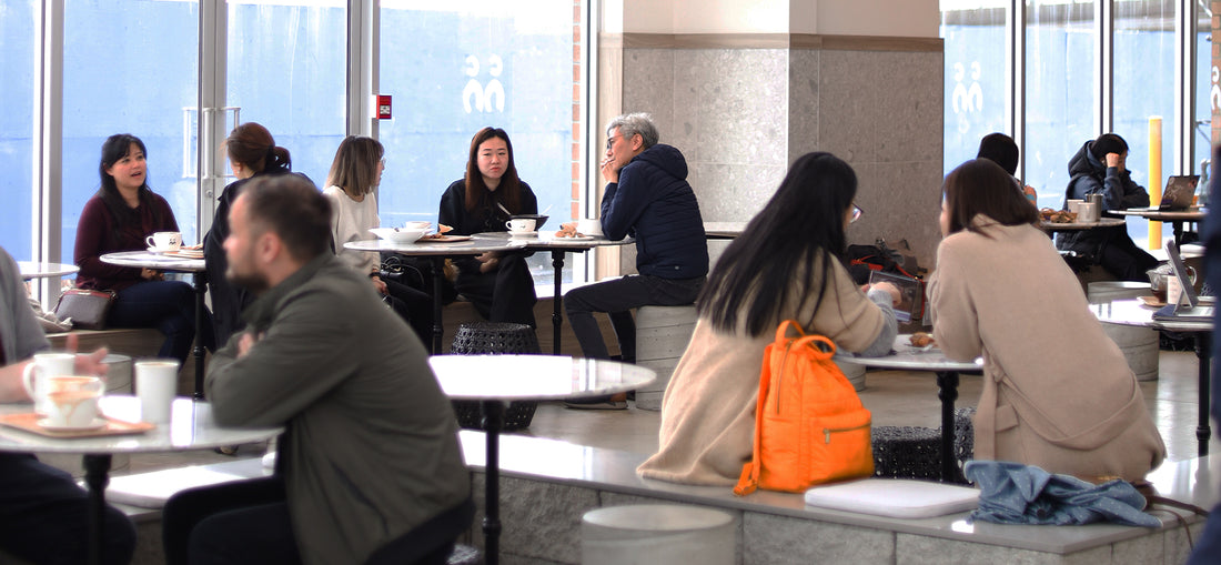 A bustling café scene at C Market Coffee, with a lively crowd of people enjoying their coffee, meals, and conversations in a vibrant, energetic atmosphere.